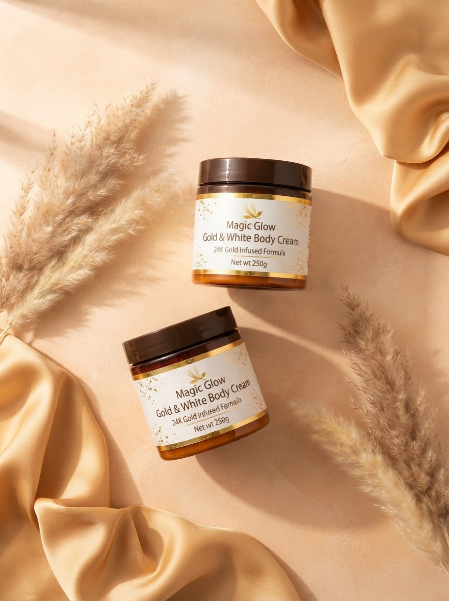 Two jars of Magic Glow Gold and White Body Cream displayed on a warm peach and honey colored surface with silk and dried bota